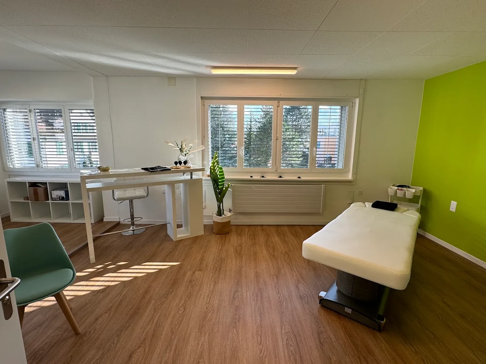 Behandlungsraum der Massagepraxis in Wil mit Massageliege und grüner Akzentwand